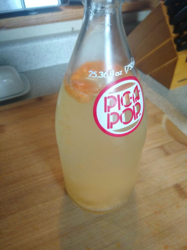 photo of a clear glass bottle with a faint yellow-tan liquid and orange foam and debris floating around the surface of the liquid