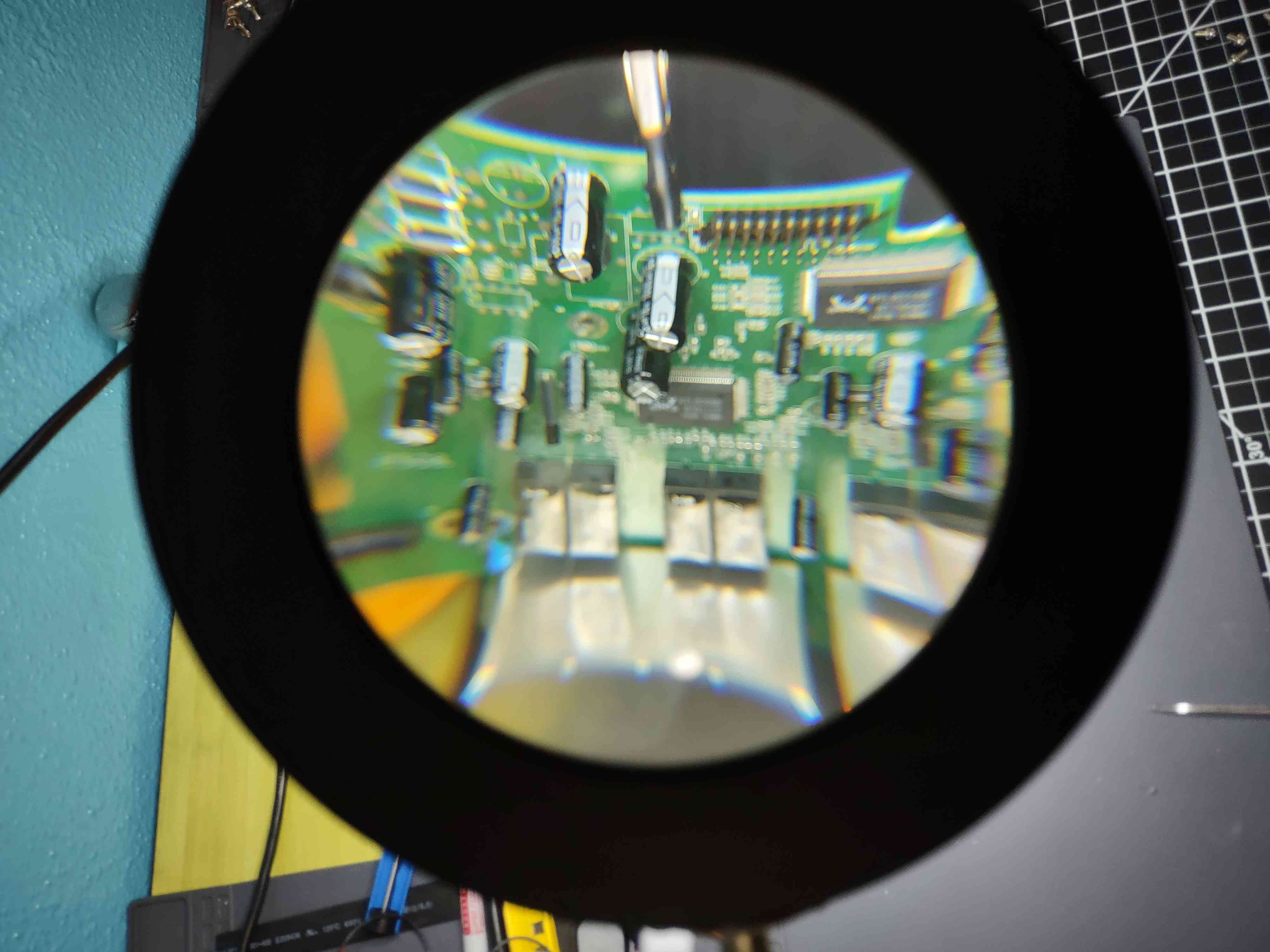 Distorted view of an ancient Ethernet switch circuitboard thru a ring light that has a built in magnification lens. This is the board I found the perfect replacement capacitor on. 