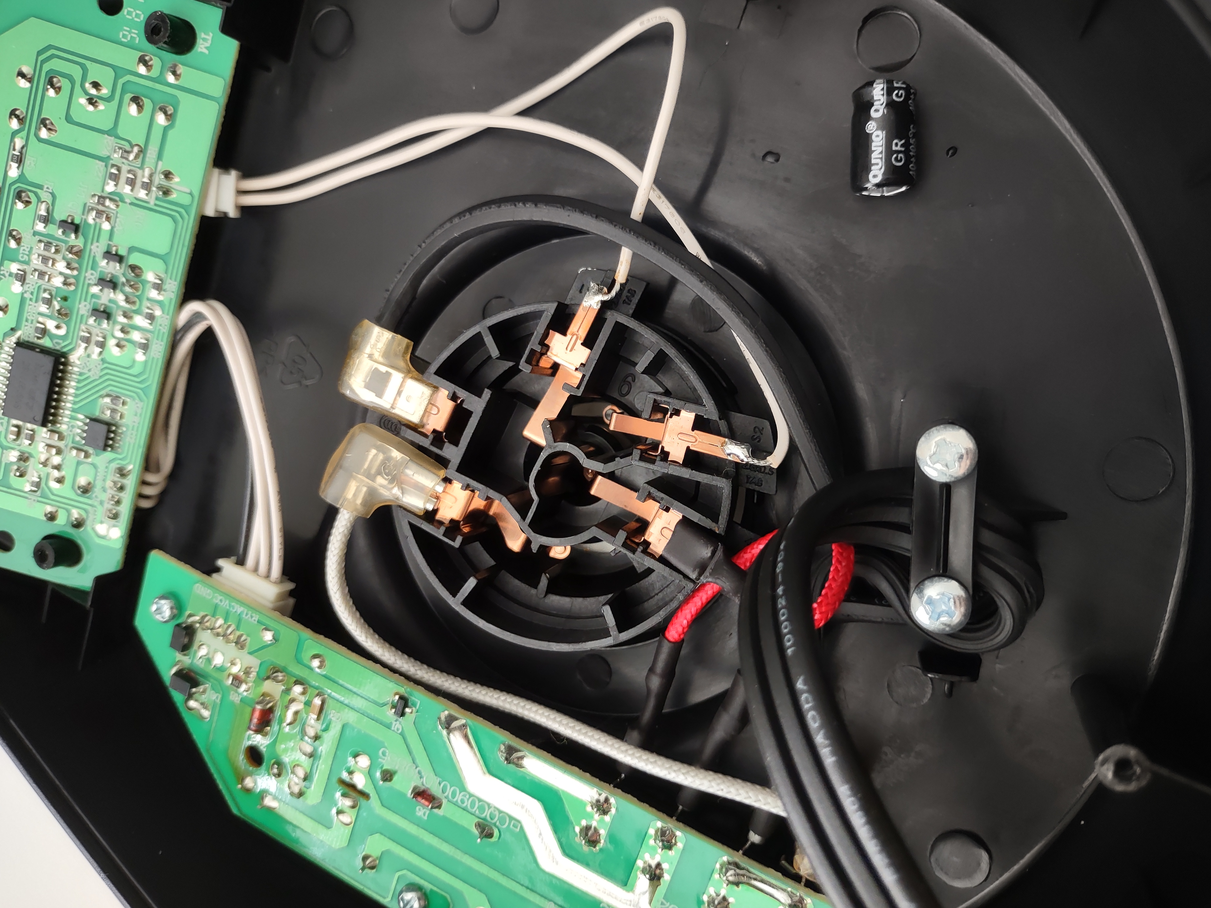 internals of the kettle, showing thick guage white, red, and black mains power wires which connect to copper coated spring steel contactors that interface with the removable kettle. Two separate circuit boards. The Power Electronics board is screwed into the plastic base with Phillips head screws